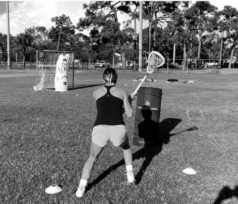 Athlete practicing a lacrosse shooting drill on a grass field.