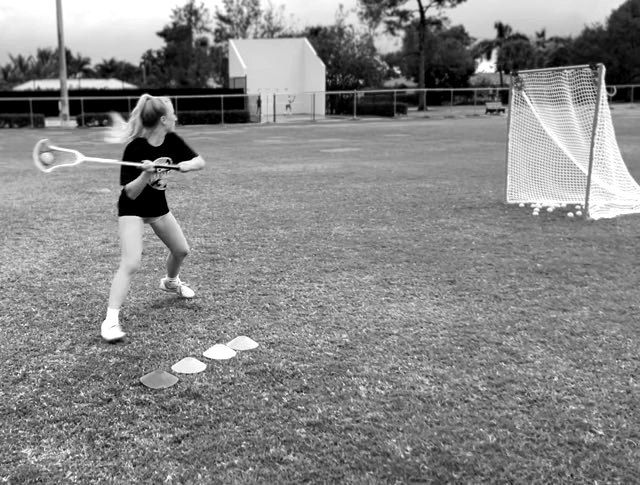 Athlete throwing a lacrosse ball toward a goal during a field drill.