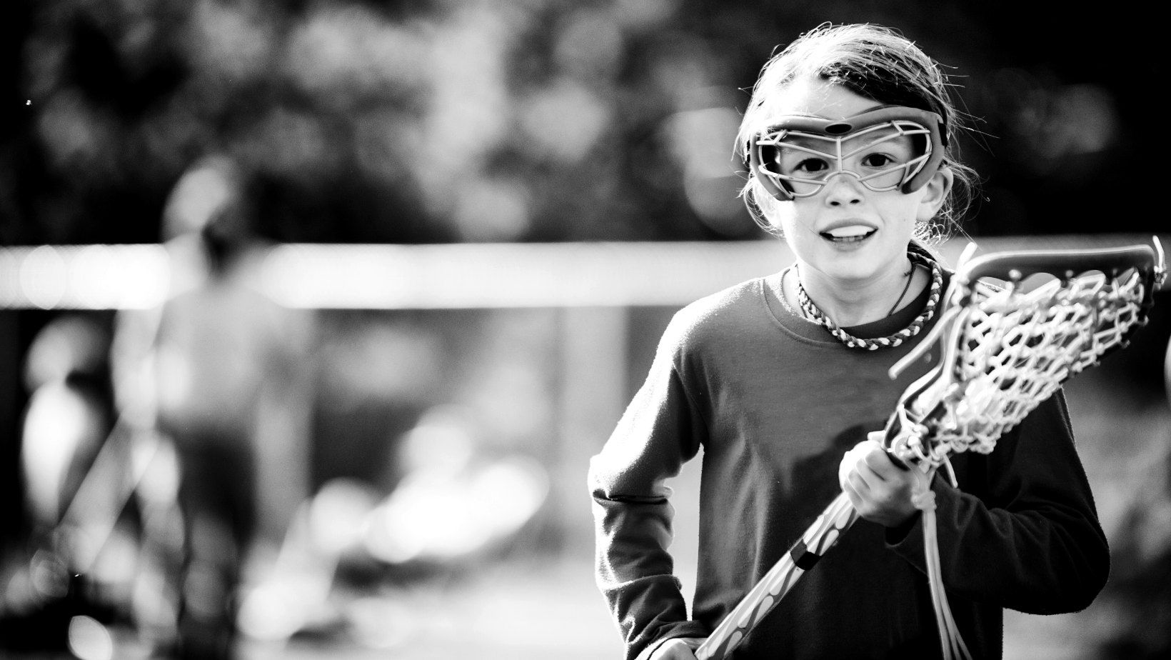 Black and white photo of a youth lacrosse player in goggles cradling a stick.