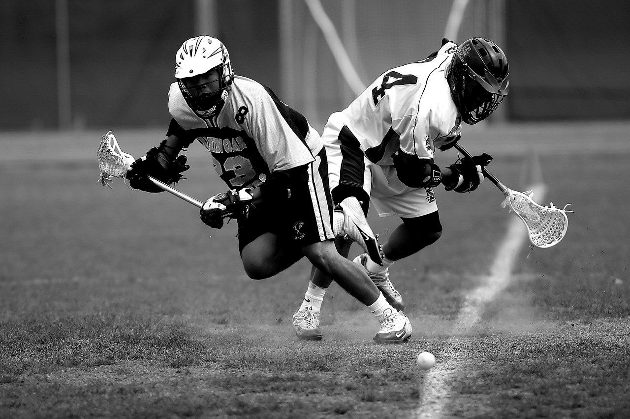 Two lacrosse players battling for a ground ball, in black and white.