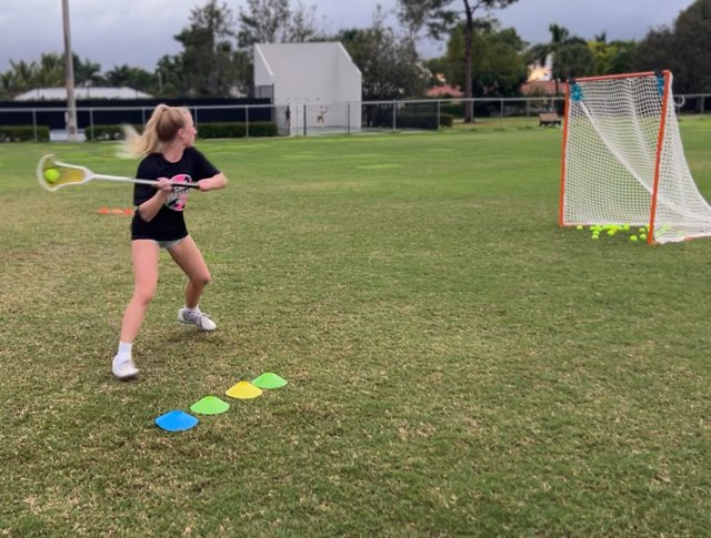 Athlete throwing a lacrosse ball toward a goal during a field drill.